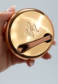 Rund, polert beholder i roségull med preget logo og festet flat skje. Glatt tekstur, minimalistisk design og blank finish.