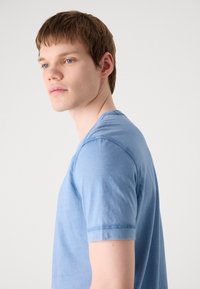 Camiseta azul de manga curta feita de algodão suave. Apresenta um decote redondo e detalhes de costura discretos. Textura suave com um ajuste descontraído.