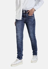 Tunna denimjeans i en mörkblå tvätt, med femfickorsdesign, lätt blekning och silverfärgade knappdetaljer, i kombination med vita sneakers.