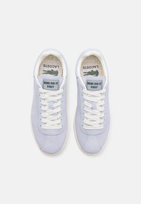 Baskets Lacoste en cuir suédé lavande clair avec des lacets blancs, dotées d'une étiquette rectangulaire sur la languette indiquant "RENE DID IT FIRST." Semelles intérieures texturées.