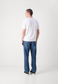 Korte mouw witte t-shirt gecombineerd met blauwe denim jeans. De jeans hebben een relaxte pasvorm en bevatten twee achterzakken met stiksels.