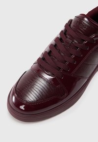 Burgundy värvi tenniset, mis sisaldavad lakknahka ja tekstuurilisi aktsente, ümar varvas, tugevdusõmblused ja paeltega kinnitamine.