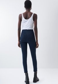 Höga, mörkblå skinny jeans med en slät yta och bakfickor, kombinerade med en åtsittande vit linne och svarta ankelsningar.