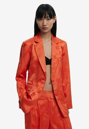 Oranje satin jasje met bloemenborduursel, voorzien van een enkele knoopsluiting, gezakte revers en voorzakken, gecombineerd met bijpassende broek.