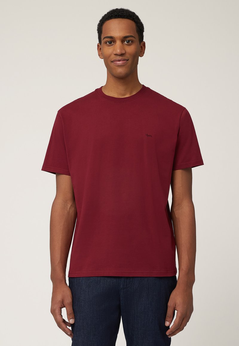 T-shirt in cotone borgogna con collo a giro e maniche corte, con un piccolo logo nero sul lato sinistro del petto, abbinato a jeans in denim scuro.