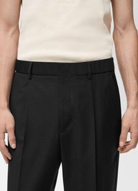 Pantalones ajustados negros con una textura suave, con frente plano, presillas para cinturón y bolsillos laterales, combinados con una camiseta sin mangas de color claro.
