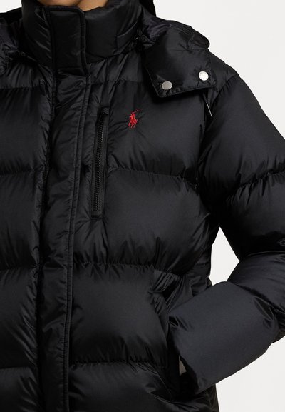 Black puffer jacket with a high collar, featuring quilted sections, a zippered chest pocket, and a red logo accent on the chest.