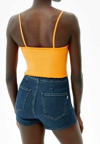 Orange ribbed crop top with scalloped edges, paired with high-waisted dark blue denim shorts featuring front and back pockets.