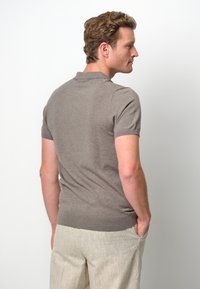 Kortärmad pikétröja i dämpad brun tyg, med ribbad krage och ärmslut, figursydd design, tillsammans med ljusbeige linnebyxor.