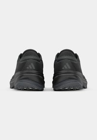 Paar schwarze Sportschuhe von hinten betrachtet, zeigt strukturierte Sohlen und Logo auf der Fersenkappe vor weißem Hintergrund.