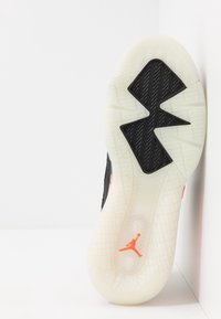 Sole basketbalové obuvi, obsahující černý gumový vzor s bílým protiskluzovým povrchem a oranžovým logem Jumpman uprostřed.