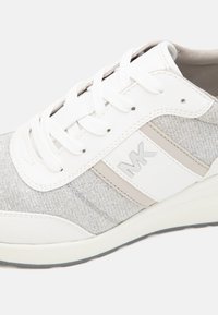 Sneaker bianco con tessuto texturizzato grigio chiaro, caratterizzato da un design mid-top, lacci piatti e un logo in rilievo su un pannello laterale.