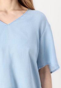 Top azzurro chiaro a maniche corte con scollatura a V. Realizzato in tessuto morbido con una superficie liscia e una cucitura sottile lungo il colletto.