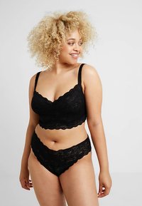 Braletă neagră din dantelă cu margini ondulate și bretele reglabile, combinată cu chiloți din dantelă asortați, cu talie înaltă. Aspect moale, texturat.