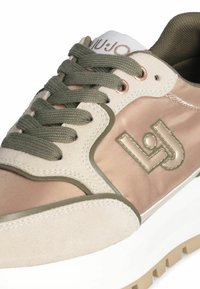 Baskets beiges et roses en satin et daim, avec des lacets verts, une semelle blanche et un logo avec un léger éclat.