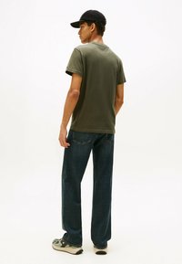 Camiseta de algodón verde oliva, de manga corta, con cuello redondo; combinada con vaqueros de pierna recta azul oscuro y zapatillas grises con detalles en verde.