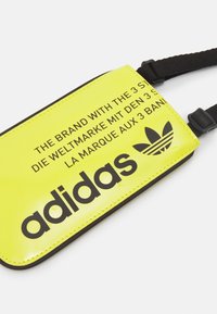 Gul vattentålig påse med svart text och logotyp. Har en justerbar svart rem och mjuk yta. Måtten passar små föremål.