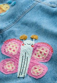 Denim kangas, millel on suur, värvikas liblikapilt roosa ja sinisega, ruuduliste mustritega, kontrastse õmblusega ääristatud.