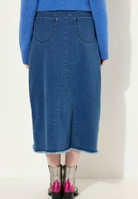 Falda midi de mezclilla en azul, con abertura en la parte posterior, dobladillo deshecho y dos bolsillos en la parte trasera. Combinada con botas metálicas hasta el tobillo con acentos en rosa.