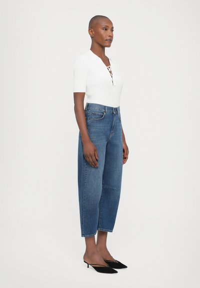 Hvid ribbet top med korte ærmer og snøre-nakkeudskæring, parret med højttaljede blå denim bukser med bred ben og sorte spidse hæle.