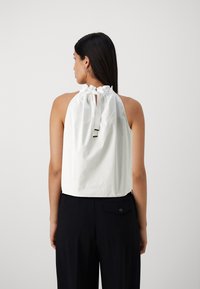 Bílý halter top s nabíraným výstřihem a detailem ve tvaru klíčové dírky na zadní straně, kombinovaný s černými kalhotami s vysokým pasem. Hladká textilie.