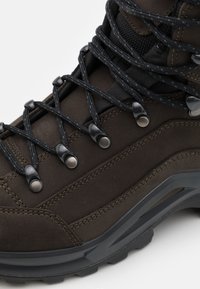 Brauner Leder-Wanderstiefel mit schwarzen Schnürsenkeln, Metallösen und strukturierten Akzenten. Verfügt über eine robuste schwarze Gummisohle und verstärkte Nähte.