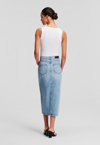 Modra jeans srednje dolžine s prilegajočim pasom, dvema zadnjima žepoma in vezenimi detajli. Kombinirana z belo brezrokavno majico in črnimi petkami.
