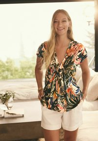 Bloemenprint, short-sleeve top in levendige kleuren met een diepe V-hals en geraffineerde details. Gepaard met witte shorts.