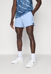 Lyseblå træningsshorts med sidepaneler i mesh, parret med en blå tie-dye tanktop. Hvide sneakers og sokker fuldender outfittet.