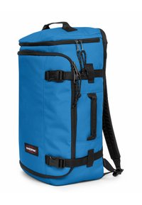 Blå tygryggsäck med svarta detaljer, utrustad med ett handtag ovanpå, justerbara axelremmar, dragkedjor och en sidoficka med spänne.