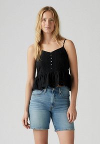 Top peplum nero con spalline regolabili, con chiusura a bottoni e bordo in pizzo. Abbinato a pantaloncini di jeans azzurri chiari.