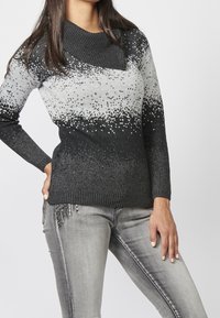 Pull en tricot avec un large col noir, un motif dégradé gris et des accents de paillettes légères. Associé à un jean gris ajusté.