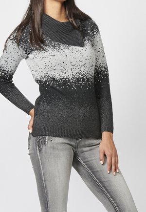 Pull en tricot avec un large col noir, un motif dégradé gris et des accents de paillettes légères. Associé à un jean gris ajusté.