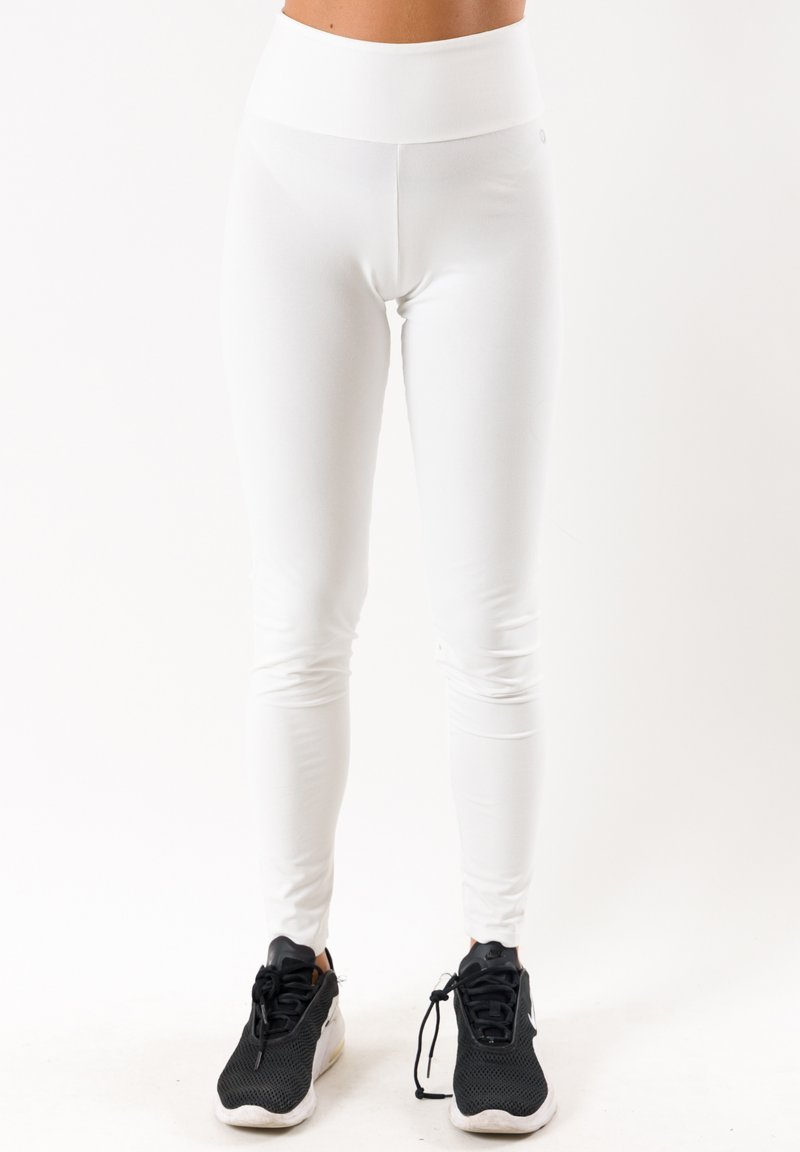 Leggings blancos de cintura alta, fabricados con un material elástico, que presentan una textura suave y un diseño ajustado, combinados con zapatillas deportivas negras.