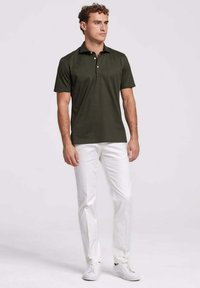 Donkergroen polo-shirt met een puntkraag, twee knopen, gecombineerd met witte broek en witte sneakers. Glad textuur.