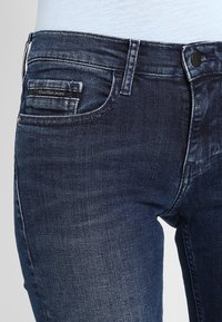 Tummat farkut ovat slim fit -malliset, keski- korkealla vyötäröllä ja niissä on hieno haalistuminen. Takapocketissa on brändin logo.