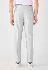 Helles graue, maßgeschneiderte Hose mit glatter Textur, ausgestattet mit zwei Gesäßtaschen mit Knöpfen und einem geraden Schnitt. Getragen mit weißen Sneakers.