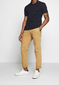 Polo navy avec un col classique, associé à un chino beige et des baskets blanches avec une accent noir. Tissu lisse et coupe ajustée.