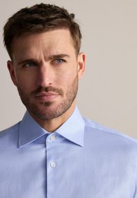 Cămașă cu model de culoare albastru deschis, cu guler tip spread, două butoane în față și un finisaj din stofă texturată. Accent pe detaliile gulerului și materialului.