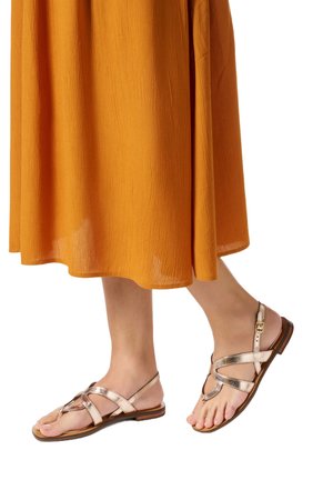 Piedi con sandali piatti con cinturini color oro rosa metallizzato abbinati a una gonna midi fluente di colore giallo senape.