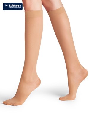 Jambes portant des bas de compression beige mi-mollet avec orteils et talons renforcés, un pied à plat et l'autre sur la pointe des orteils.