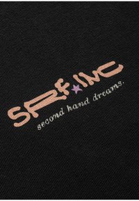 Czarna tkanina z haftowanym napisem "SFR*INC" w jasnoróżowym kolorze oraz "second hand dreams." w białym. Projekt zawiera akcent w kształcie gwiazdy w fioletowym kolorze.