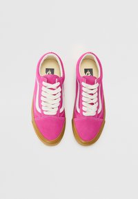 Baskets en suède rose avec des rayures blanches sur les côtés, ornées de lacets blancs et d'une semelle en caoutchouc marron. Texture lisse et design classique.