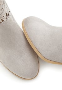 Graue Wildleder-Stiefeletten mit glatter Textur, runder Spitze und dekorativem Ausschnitt-Design am Knöchel. Mit einer hellen Gummisohle.