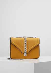 Borsa a tracolla in pelle gialla con pattina in camoscio, tracolla in catena argentata e design triangolare unico. Presenta un dettaglio di chiusura metallica.