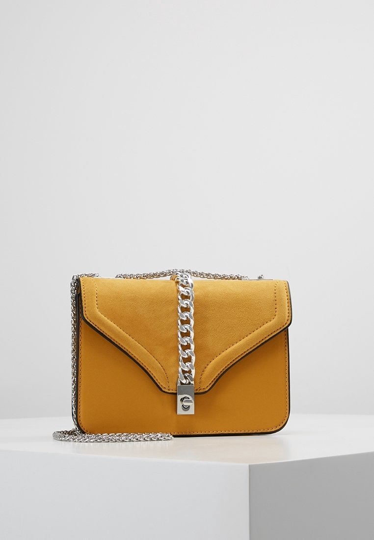 Borsa a tracolla in pelle gialla con pattina in camoscio, tracolla in catena argentata e design triangolare unico. Presenta un dettaglio di chiusura metallica.