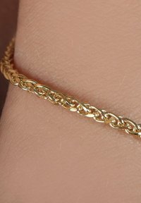 Goldene Kettenarmband mit ineinander verschlungenen ovalen Gliedern, die eine polierte Oberfläche und eine glatte Textur auf der Haut zeigen.