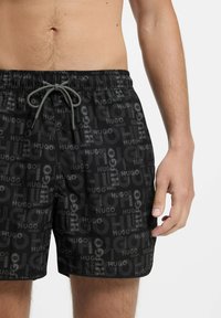 Mustat uimalyhikset, joissa on toistuva logo-kuvio. Suunnittelussa on joustava vyötärö, jossa on nauhakujan. Sileä pinta, polvipituinen leikkaus.