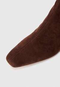 Barna suede bokacsizma hegyes orral, látható varrásokkal és sima felülettel. A dizájn illeszkedő és korszerű.