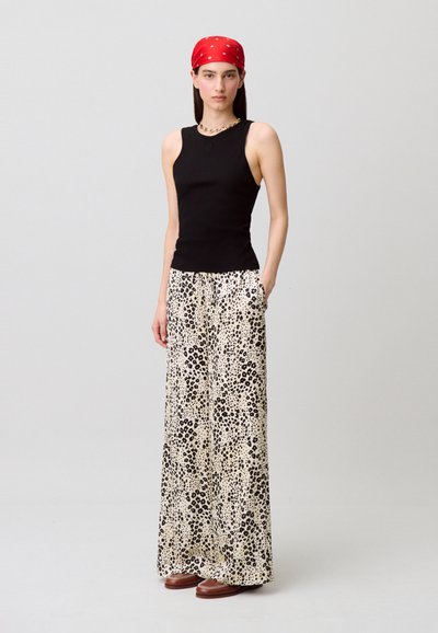 Top negro sin mangas combinado con pantalones anchos de estampado de leopardo en crema y negro. La modelo lleva un pañuelo rojo y zapatos marrones.